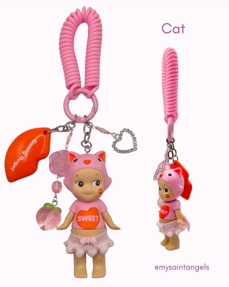 Puede incluir: Llavero rosa con una mu&ntilde;eca con tem&aacute;tica de gato, con una correa de mu&ntilde;eca en espiral rosa. La mu&ntilde;eca lleva una camiseta rosa con "SWEET", una falda rosa y una capucha con orejas de gato. Incluye un dije con el texto "Sonny Angel".