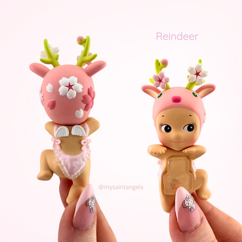 May include: Two pink Reindeer figurines with floral accents. One figurine has a pink head with white flower details and a pink outfit. The other figurine has a pink hat with flower details and a pink outfit.