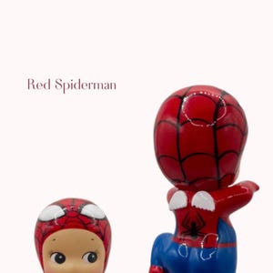 May include: Two red and blue Spiderman figurines. One is a baby-like doll with a red Spiderman mask and outfit. The other is a Spiderman figure with a red head and torso, blue trousers, and white web details.