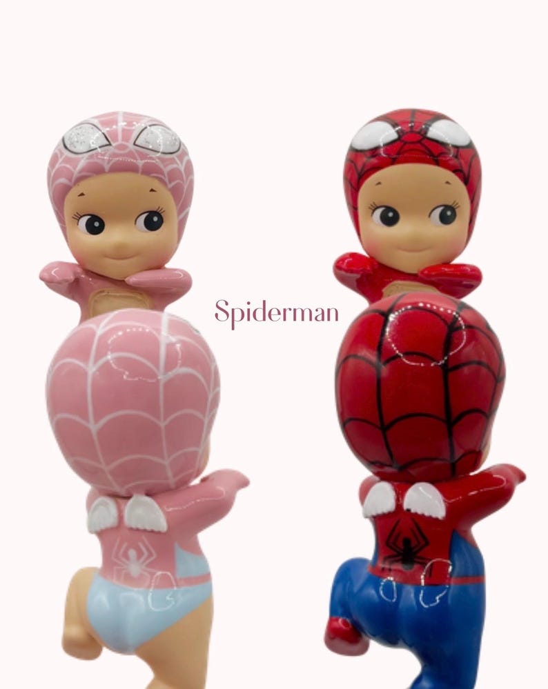 May include: Two figurines of a baby dressed as Spiderman. One is pink with a light blue diaper, the other is red and blue. The text "Spiderman" is in the centre of the image.
