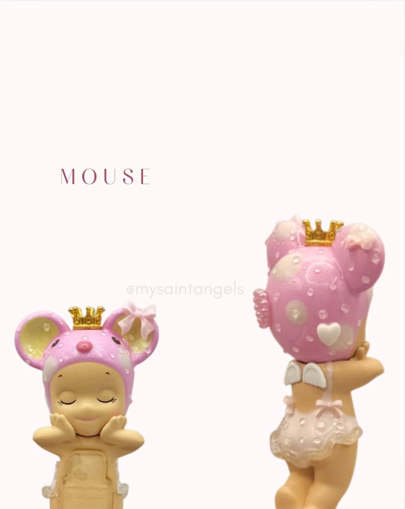 May include: Two pink mouse figurines with golden crowns. The figurines have a light pink and white polka dot design on their heads and ears. The word "MOUSE" is printed in the upper left corner.