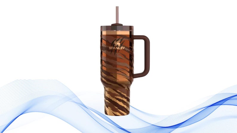 Puede incluir: Un vaso Stanley con un dise&ntilde;o de rayas de tigre marr&oacute;n. El vaso tiene un asa, una pajita y el logotipo de Stanley. El vaso est&aacute; dise&ntilde;ado para mantener las bebidas fr&iacute;as o calientes. Es una botella de agua reutilizable.