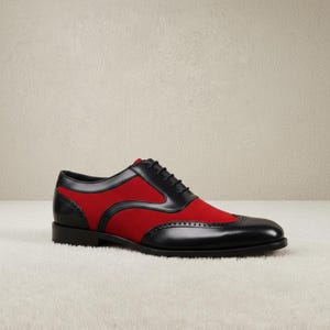 Close-up of black leather wingtip brogue perforations and crimson red contrast panels on men's lace-up oxford dress shoes, showing woven black laces and rounded toe