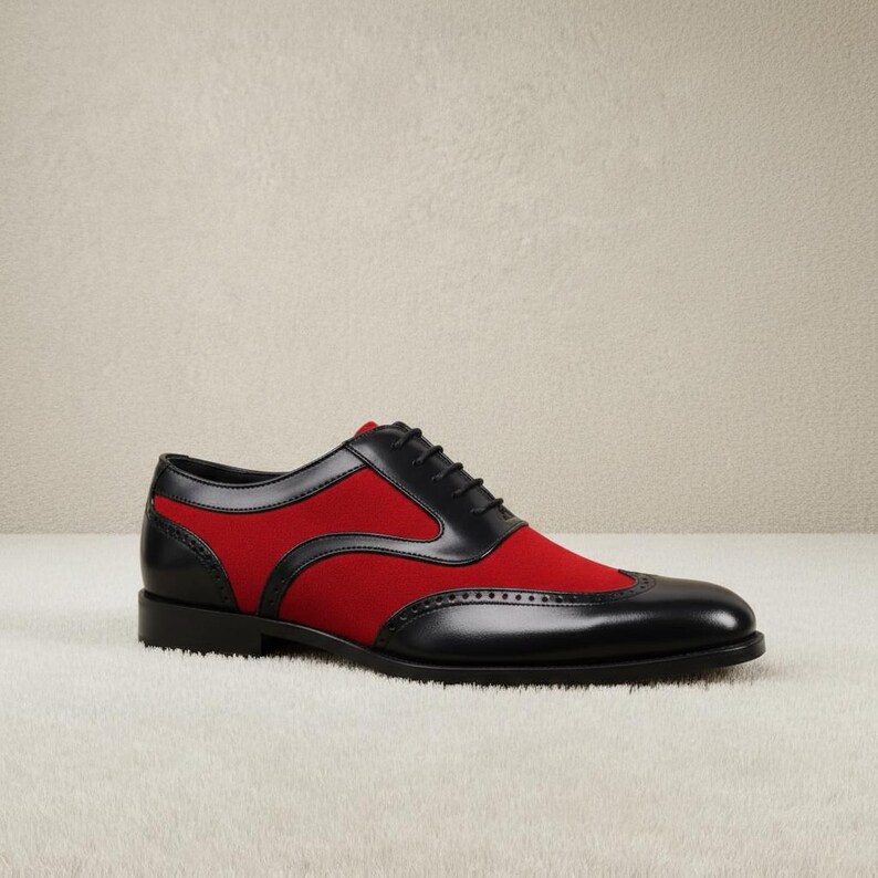 Close-up of black leather wingtip brogue perforations and crimson red contrast panels on men's lace-up oxford dress shoes, showing woven black laces and rounded toe