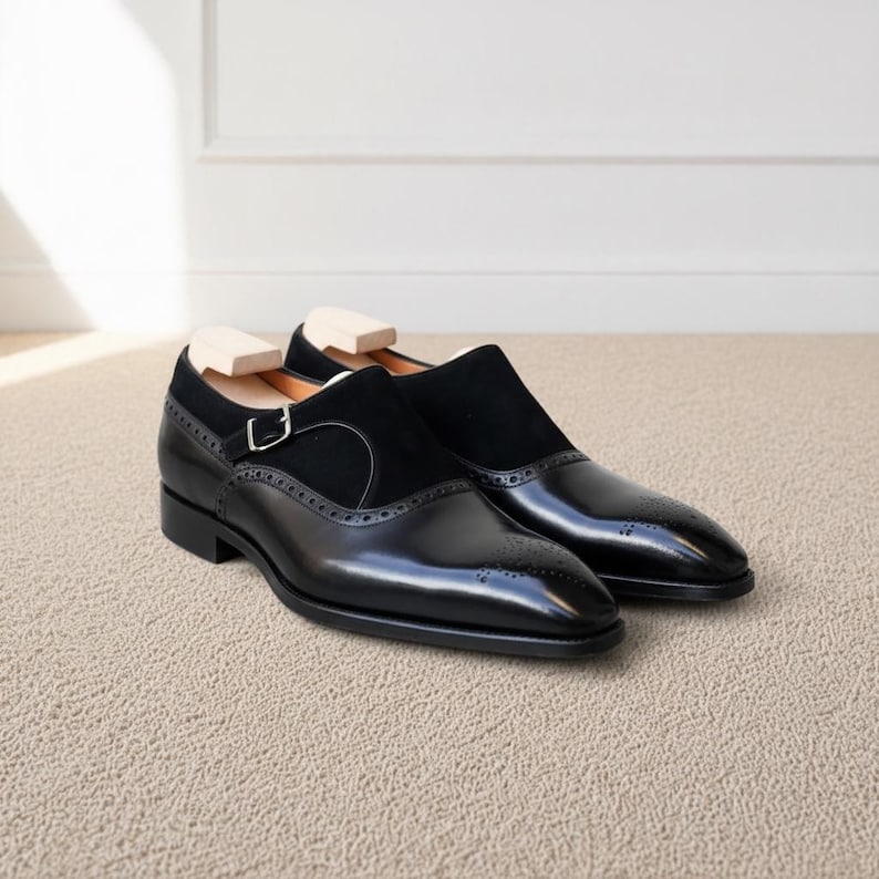 Pair of black monk strap loafers with polished leather finish on beige carpet background