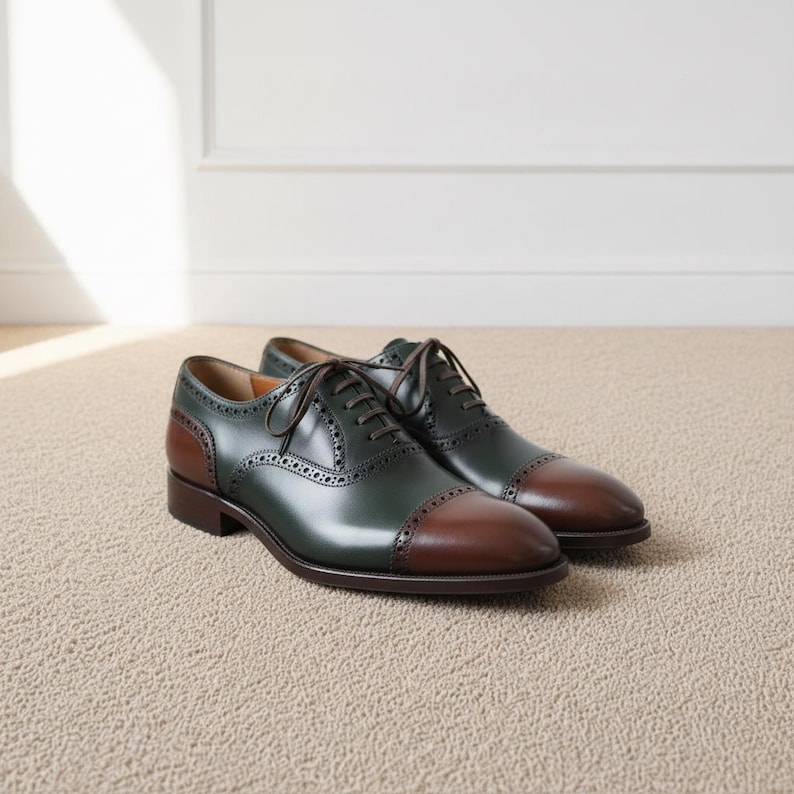 Pair of green and brown cap toe oxford shoes with brogue detailing on beige carpet