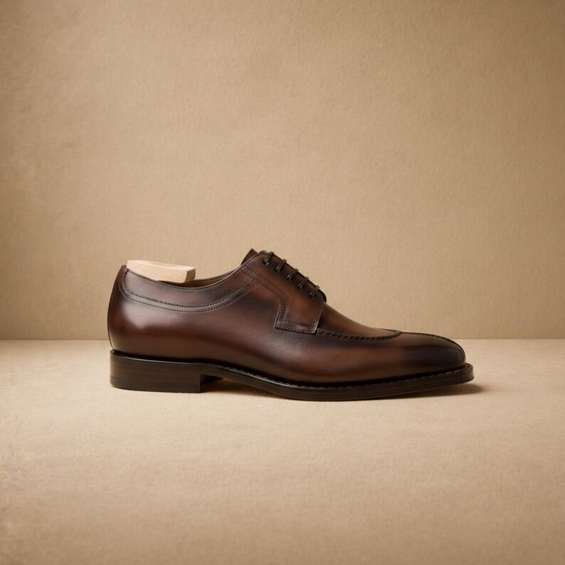 May include: A brown leather dress shoe with a split-toe design. The shoe features a classic lace-up closure and a wooden shoe tree inside. The leather has a polished finish, and the sole is black. The shoe is approximately 12 inches long.