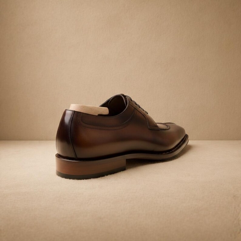 May include: A brown leather dress shoe with a cap toe design. The shoe has a polished finish and a wooden shoe tree inside. The heel is approximately 1 inch high. The shoe is displayed on a neutral background.