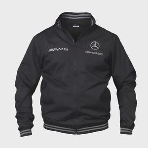 May include: Black zip-up jacket with the AMG logo on the left chest and the Mercedes-Benz logo on the right. The jacket has a stand-up collar and striped detailing on the cuffs and hem. A sporty, casual jacket.