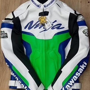 Könnte beinhalten: Weiße, grüne, blaue und schwarze Kawasaki Ninja Motorradjacke. Die Jacke trägt das Wort "Kawasaki" am Kragen und an den Ärmeln sowie das Wort "Ninja" in Blau auf der Brust. Ein Lederetikett ist angebracht.