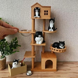 Könnte beinhalten: Ein Miniatur-Katzenbaum aus Holz mit mehreren Ebenen, auf dem sich mehrere schwarz-weiße Katzenfiguren befinden. Der Katzenbaum hat ein hausförmiges Oberteil und eine kleine Futterschale. Die Katzen befinden sich in verschiedenen Posen und sorgen für einen verspielten Touch.