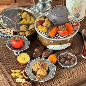 以下が含まれることがあります： ピーナッツ、クルミ、柿、サツマイモなど、さまざまな食品を展示したミニチュアフードディスプレイ。漫画の顔が付いた小さな茶色のグリルには、食べ物がいくつか入っています。商品は小さなプレートに並べられています。