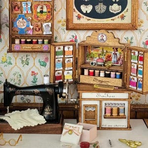 May include: A detailed miniature sewing room scene. It features a black Singer sewing machine, wooden cabinets filled with thread spools, and a shop sign reading "Fil au chinois". The scene includes various sewing accessories and decorative elements.