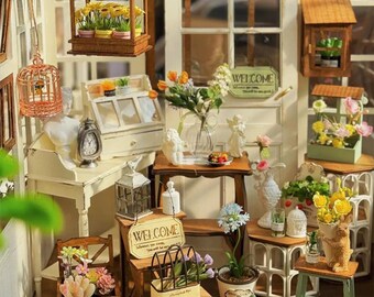 May include: Miniature garden scene with a variety of decorative elements. Includes small wooden structures, potted plants, angel figurines, and a "WELCOME" sign. The scene is set against a white door with a window.