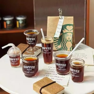 Peut inclure: Divers types de mini-boissons au café dans différents styles de verre, dont un verre à pied, un grand verre et une petite tasse avec un couvercle. Chaque verre porte l'inscription "COFFEE BRINGS TOGETHER". Un sac de café Starbucks est en arrière-plan.