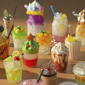 Op de afbeelding: Een verzameling miniatuur, kleurrijke dessertdranken. De drankjes hebben verschillende toppings zoals slagroom, fruitschijfjes en snoep. Sommige hebben rietjes en andere zitten in decoratieve glazen. Het algemene thema is een grillige, speelse esthetiek.