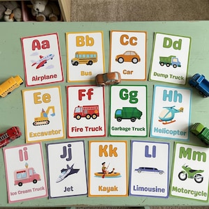 May include: A set of thirteen educational alphabet cards featuring illustrations of vehicles from A to M, including an airplane, bus, car, dump truck, excavator, fire truck, garbage truck, helicopter, ice cream truck, jet, kayak, limousine, and motorcycle.