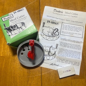 May include: A Dexter's Wool Cutter for latch hook rug work, catalog number 19-01065. The set includes a grey plastic tool with a red handle, a green and white cardboard box, an instruction sheet, and a small rectangular blade holder box.