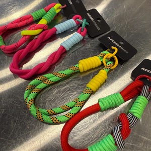 May include: Close-up of colorful rope accessories. The ropes are in various colors, including pink, green, yellow, and red. Each rope has a loop and a clasp. The accessories are displayed on a metallic surface, with black tags that read "ACCESSORIES".