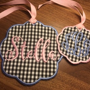 May include: Two fabric gift tags with scalloped edges. One tag is black and white gingham with the name "Stella" embroidered in pink. The other tag is black and white gingham with a monogram embroidered in blue.