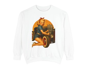May include: White sweatshirt featuring a vintage-style illustration of a woman in denim shorts and a top, kneeling beside a classic car. The artwork has a retro aesthetic with a warm color palette and a circular background.