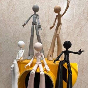May include: Five articulated stick figure dolls in gray, tan, white, light pink, and black. Each doll features a spherical head, slender limbs, and flared feet. They are posed in various positions, with some standing and others sitting on a yellow object.