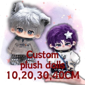 May include: Two plush dolls with detailed facial features and hair. The left doll has grey hair and ears, wearing a grey sweater with 'LONDON' text and plaid pants. The right doll has purple hair with a star accessory, wearing a white top and a small bag.