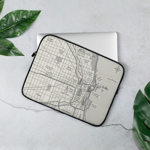 Könnte beinhalten: Eine rechteckige Laptoptasche mit einer schwarz-weißen Karte von Chicago, Illinois. Die Karte zeigt beschriftete Wahrzeichen wie The Loop, Navy Pier, Wrigley Field und den Lake Michigan sowie eine Windrose in der oberen rechten Ecke.