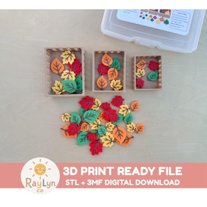 May include: Three rectangular brown plastic crates containing small, flat, leaf-shaped pieces in red, orange, yellow, and green. A loose pile of identical leaf-shaped pieces is arranged below the crates. A clear plastic storage container is visible.