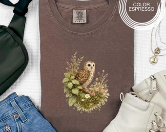 May include: Espresso-coloured t-shirt with an owl illustration surrounded by flowers and leaves. The shirt is Comfort Colors brand. The image also shows a green bag, blue jeans, white boots, and sunglasses. The text on the image says 'Color Espresso'.
