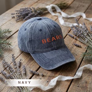 May include: Navy blue baseball cap with the word "BEARS" embroidered in orange. The cap is made of a washed cotton material and has a curved brim. The word "NAVY" is printed at the bottom of the image.