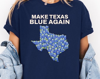 May include: Navy blue t-shirt with the phrase "MAKE TEXAS BLUE AGAIN" in white block letters. The state of Texas is filled with a blue and green floral pattern. The shirt is a classic crew neck.