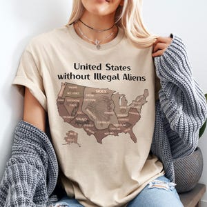 K&ouml;nnte beinhalten: Beiges T-Shirt mit dem Text "United States without Illegal Aliens" &uuml;ber einer Karte der Vereinigten Staaten. Die Karte zeigt verschiedene indianische St&auml;mme. Das T-Shirt hat eine neutrale Farbe.