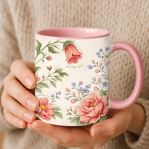 Könnte beinhalten: Keramikbecher mit rosa Griff und Innenraum. Der Becher ist mit einem Blumendesign in Rosa, Rot und Blau mit grünen Blättern und dem Text "no kings here" und "no throne forever" verziert.