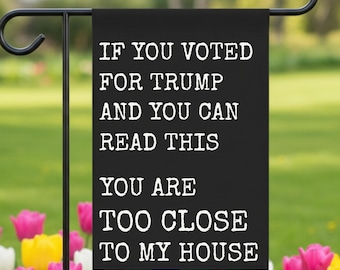 May include: A black garden flag with white text that reads: "IF YOU VOTED FOR TRUMP AND YOU CAN READ THIS YOU ARE TOO CLOSE TO MY HOUSE." The flag is hanging on a black metal stand, with a garden of colorful tulips in the foreground.
