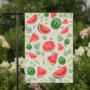 May include: A decorative garden flag featuring a watercolor design of watermelons and leaves on a light gray background. The flag displays whole watermelons, watermelon slices, and seeds, creating a summery, fruit-themed pattern.