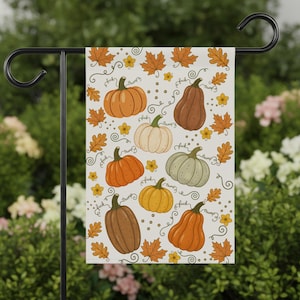 Peut inclure: Un drapeau de jardin rectangulaire présentant un motif répétitif de diverses citrouilles dans des tons orange, marron, blanc et vert, parsemé de feuilles d'automne, de petites fleurs jaunes et du texte manuscrit répété fuck trump.