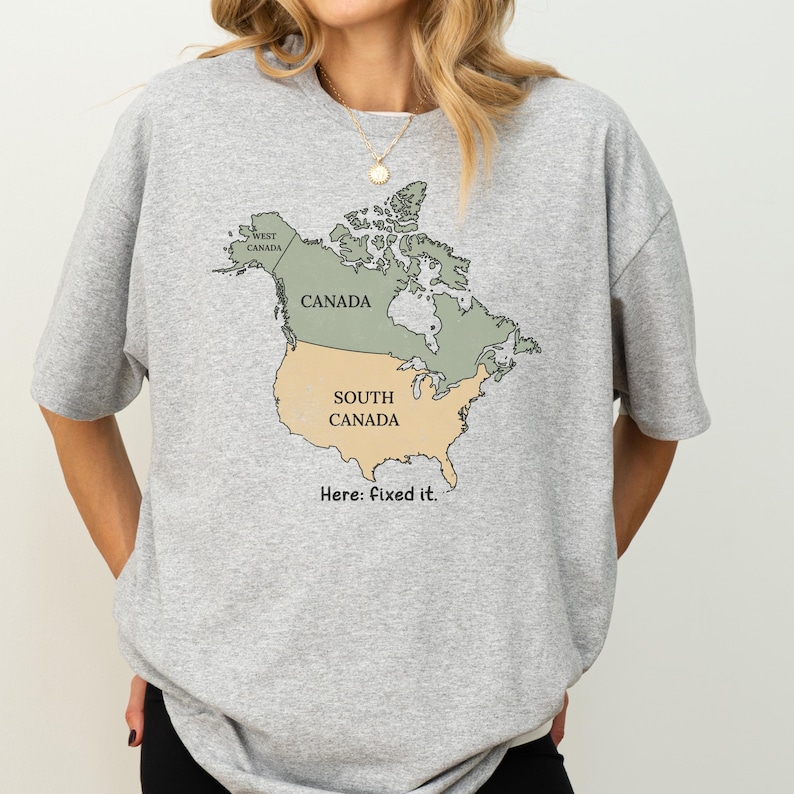 May include: A heather grey t-shirt featuring a graphic of the North American continent. The map is divided into two sections: the northern portion labeled Canada and the southern portion labeled South Canada. The text Here: fixed it. is below.