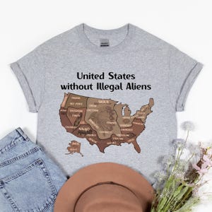 K&ouml;nnte beinhalten: Hellgraues T-Shirt mit dem Text "United States without Illegal Aliens" &uuml;ber einer braunen Karte der USA. Die Karte zeigt die Namen verschiedener indianischer St&auml;mme.