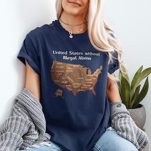 K&ouml;nnte beinhalten: Marineblaues T-Shirt mit dem Text "United States without Illegal Aliens" &uuml;ber einer braunen Karte der Vereinigten Staaten. Die Karte enth&auml;lt die Namen der amerikanischen Ureinwohner. Das T-Shirt wird getragen.