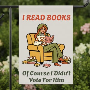 May include: A garden flag with the text "I READ BOOKS" in red. The flag features an illustration of a person reading a book while seated in a yellow armchair. The text "Of Course I Didn't Vote For Him" is below the illustration.