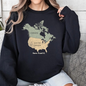 May include: A black long-sleeve sweatshirt featuring a graphic of the North American continent. The map is divided into sections labeled West Canada, Canada, and South Canada. Below the map, the text reads: Here: fixed it.