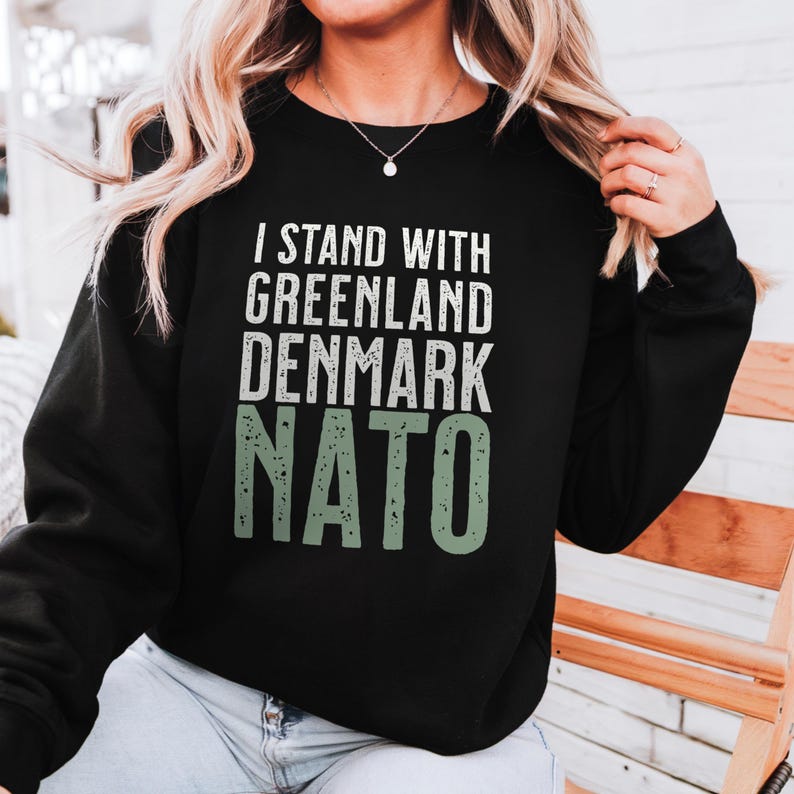 Op de afbeelding: Zwart sweatshirt met de tekst "I STAND WITH GREENLAND DENMARK NATO" in wit en groen. De tekst is in een vetgedrukte, schreefloze lettertype. De sweatshirt is een crew neck stijl en lijkt gemaakt van een zacht materiaal.