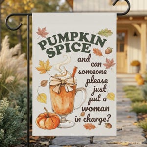 May include: A rectangular garden flag with a cream background featuring a watercolor illustration of a glass mug filled with a pumpkin spice beverage, topped with whipped cream and a cinnamon stick, surrounded by autumn leaves and a pumpkin.