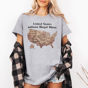 K&ouml;nnte beinhalten: Ein graues T-Shirt mit dem Text "United States without Illegal Aliens" &uuml;ber einer braunen Karte der Vereinigten Staaten. Die Karte enth&auml;lt Staatsnamen. Die Person tr&auml;gt ein schwarz-wei&szlig; kariertes Hemd.