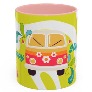 May include: A ceramic mug with a light pink interior and rim. The exterior features a lime green background with a graphic of a multi-colored van decorated with white flowers. The word "Hippy" is printed in blue script on the side of the mug.