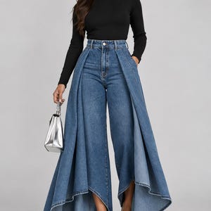 Op de afbeelding: Een zwart shirt met lange mouwen en een opstaande kraag, gecombineerd met een blauwe high-waist jeans met een aangehechte, vloeiende, tot op de grond reikende geplooide rok. De outfit is afgewerkt met een kleine zilveren handtas en zilveren pumps.