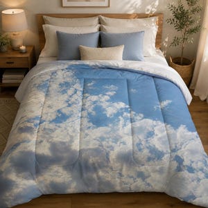 May include: A rectangular comforter featuring a photographic print of a bright blue sky filled with white, fluffy clouds. The bedding has a quilted texture with vertical stitching lines and covers the top surface of a bed with pillows.