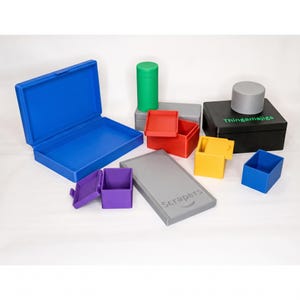 Peut inclure: Ensemble de boîtes et de conteneurs en plastique colorés de différentes formes et tailles. Comprend une grande boîte bleue, de petites boîtes rouges et jaunes, un cylindre vert et une boîte noire avec le texte "Thingamajigs". Une boîte grise avec le texte "Scrapers" est également présente.