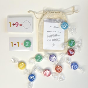 Könnte beinhalten: Lehrreiche Mathe-Lernkarten mit Gleichungen und bunten Süßigkeiten mit Zahlen. Ein Kordelzugbeutel mit Text ist ebenfalls enthalten. Der Text auf der Tasche lautet "MamaClever" und "Danke für Ihre Bestellung".